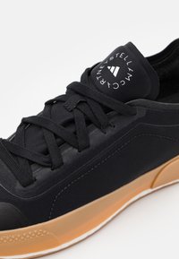 Černá atletická bota s texturovaným textilem na svršku, s tkaničkami vpředu a gumovou podrážkou. Logo na jazyku obsahuje bílé písmo a design.