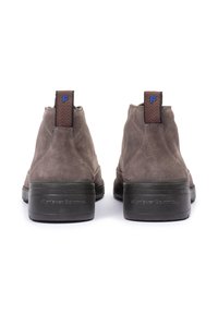 Botas de tobillo de ante gris con una pestaña marrón texturizada, logo azul y suela de goma negra, que presentan un diseño limpio y minimalista.