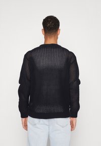 Pull en tricot noir avec un design en maille ouverte, poignets et encolure côtelés épais. Caractéristiques : coupe ample et manches longues.