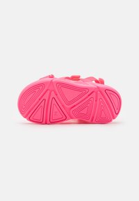 Helle pinke Sneaker-Sohle mit einem geometrischen Profilmuster. Verfügt über eine strukturierte Oberfläche und einen Riemenverschluss für einen sicheren Sitz.