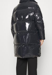 Svart, glansig pufferjacka med hög krage, med ett quiltat mönster och breda horisontella segment, knälång med långa ärmar.