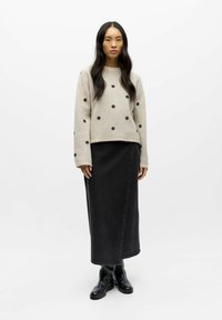 Knitted beige sweater with black polka dots, paired with a long black denim skirt and black ankle boots. Smooth texture, relaxed fit.