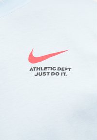 Gaiši zils īso piedurkņu T-krekls, kas izgatavots no kokvilnas. Ar sarkano Nike swoosh logo un melnu tekstu "ATHLETIC DEPT JUST DO IT."