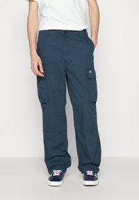 Cargo byxor i mörk marinblå färg, tillverkade av slitstark tyg, med sidofickor, lös passform och knäppning. Matchad med sneakers.