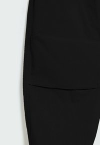 Pantalon cargo noir avec une grande poche frontale, une texture lisse et des détails cousus le long des coutures.