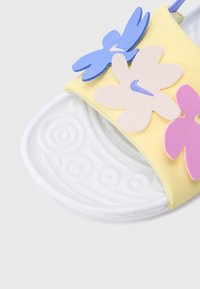 Κίτρινο σανδάλι με λου ράκι από μαλακό υλικό που διαθέτει τρεις διακοσμητικές ανθοδέσμες σε ροζ, ανοιχτό ροζ και μπλε, με υφή λευκής εξωτερικής σόλας.