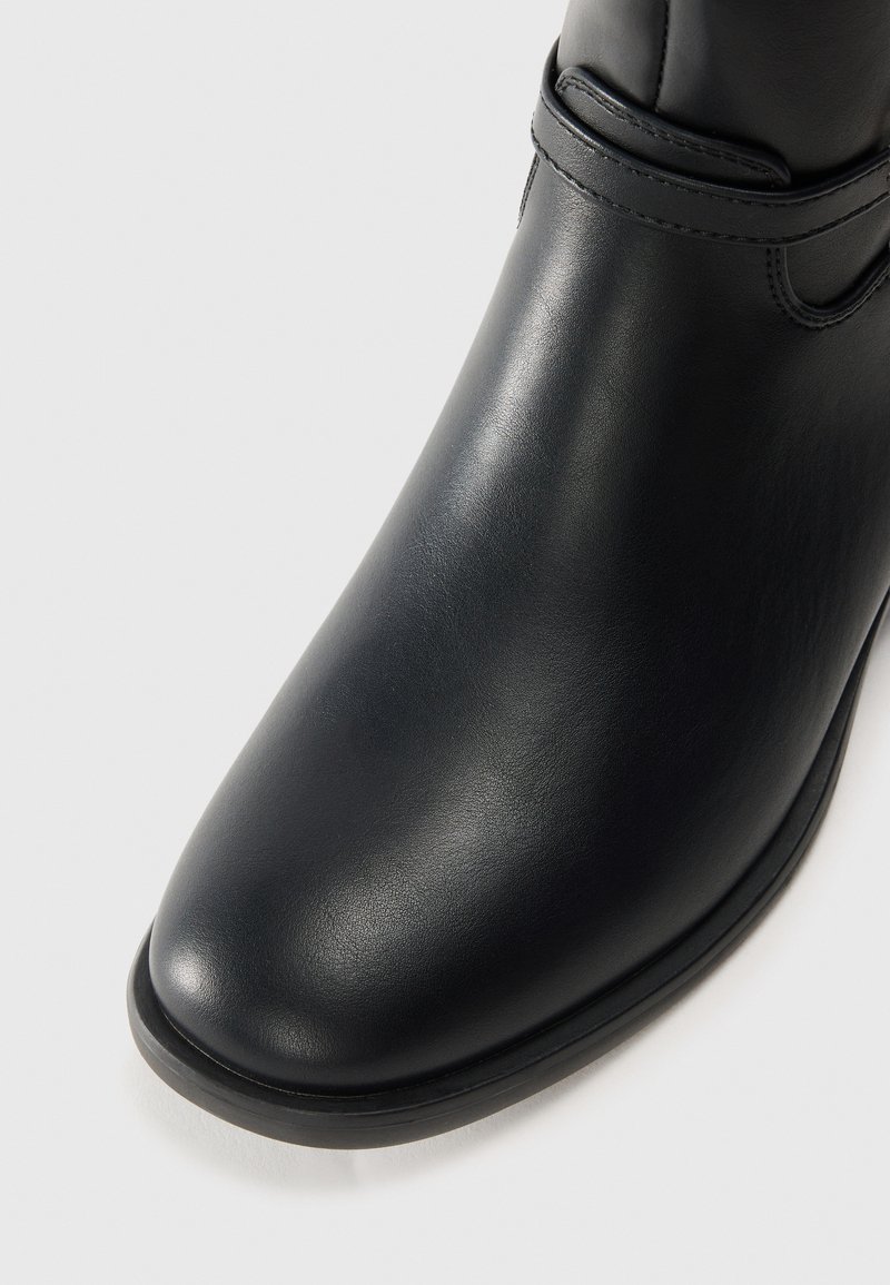 Stivale alla caviglia in pelle nera con una superficie liscia, punta rotonda e un semplice dettaglio a cinturino vicino alla caviglia. Suola piatta con cuciture sottili sui bordi.