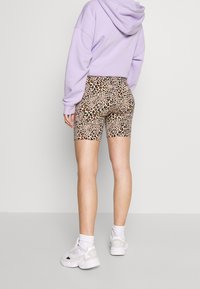 Shorts de vélo taille haute à imprimé léopard avec une base beige et des taches marron, noires et orange, associés à un sweat à capuche lilas et des baskets blanches.
