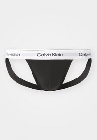Tanga nero di Calvin Klein con una morbida cintura in vita caratterizzata da testo bianco a marchio. Il tessuto è liscio, con un design minimalista e doppi spallacci.