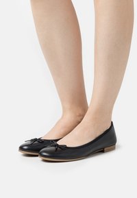 Bailarinas de piel negra con punta redonda, pequeño lazo decorativo y un bajo tacón de madera, que cuentan con un acabado suave y un diseño flexible.