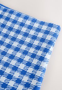 Tessuto lavorato a maglia blu e bianco con motivo pied de poule, superficie testurizzata e bordo solido blu lungo un lato.