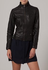 Czarna skórzana kurtka z wysokim kołnierzem, teksturowanym wykończeniem, zapięciem na suwak i bocznymi zatrzaskami. Posiada przeszycia na ramionach i przednią kieszeń.
