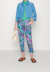 Blauw cropped jack, groene geribde top, bloemenbroek in roze en blauw, bruine slip-on sandalen en een crème handtas. Felle kleuren met patronen.