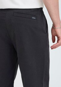 Black cotton trousers with a smooth texture, featuring back pockets and a small label. Hem is straight and design is casual.