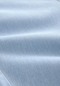 Svetlo modra denim tkanina z gladko teksturo in diagonanim tkanjem keper, ki prikazuje subtilne gube in pregibe po površini.