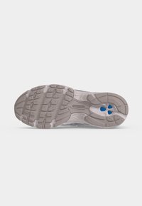 Η σόλα ενός παπουτσιού τρεξίματος New Balance με γκρι πέλμα που έχει υφή λαβής και τρεις μικρές μπλε κυκλικές λεπτομέρειες κοντά στην περιοχή της φτέρνας.