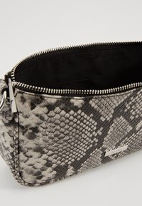 Kopertówka w szaro-czarny wzór skóry węża, wyposażona w zamek błyskawiczny i gładką podszewkę. Z metalowymi zdobieniami.