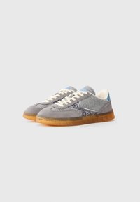 Sneaker grigie in suede con un pannello laterale scintillante, dettagli azzurri, lacci bianchi e una suola traslucida arancione. Design atletico classico.