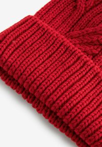 Bonnet en tricot rouge avec un motif en côtes et un large revers, fabriqué à partir de laine douce, avec une texture lisse et un design légèrement slouchy.