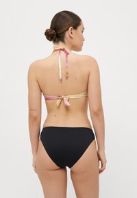 Bikini-set med et flerfarget halterneck-bånd med knytt bak og svart høy midje-bunn. Stoffet ser glatt ut med solid fargekontrast.