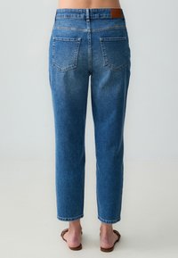 Jeans in denim blu con una vestibilità a gamba dritta, stile a cinque tasche e un'etichetta in pelle marrone in vita. Vita media, leggermente strappati.