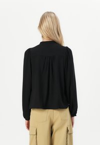 Must have pikkade varrukatega must blouse, ümmarguse krae, volditud seljadetaili ja kerge volangiga varrukate ning beežide cargo-pükstega.