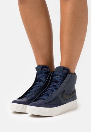 Sneaker alte navy con tomaia in pelle testurizzata, lacci piatti e una spessa suola in gomma bianca, con un accento logo nero.