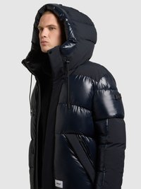 Mornarsko modra puhasta jakna z lesketajočim zaključkom, velikim kapuco, žepki z zadrgo in etiketo na robu. Prešita zasnova z elastičnimi poudarki.