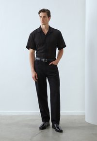 Black short-sleeve shirt with vertical stripes, paired with black trousers and shiny black shoes. Simple, clean design with a fitted silhouette.