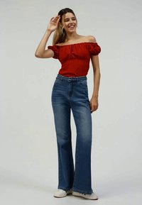 Top vermelho ombro a ombro com mangas bufantes, combinado com jeans azuis flare de cintura alta e ténis brancos. Design simples com tecido texturizado.