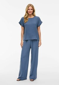Top blu, strutturato, con collo rotondo e maniche corte, abbinato a pantaloni larghi coordinati. Entrambi i capi hanno una vestibilità comoda.