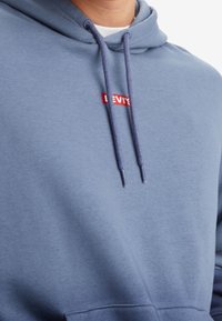 Felpa blu in cotone morbido, con un logo in testo rosso sul petto, dotata di coulisse regolabile e vestibilità comoda.