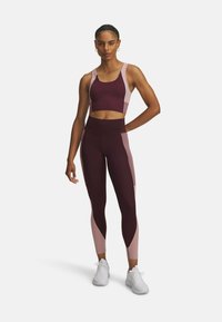 Burgunderfarbener Sport-BH kombiniert mit passenden hochgeschnittenen Leggings mit rosafarbigen Akzenten. Der Stoff scheint dehnbar und hat eine glatte Textur.