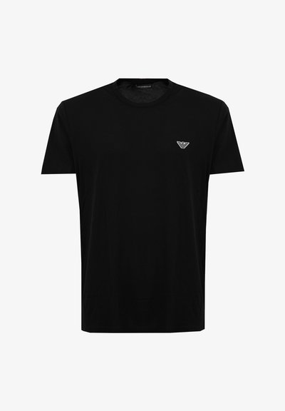 Camiseta negra de manga corta con cuello redondo y pequeño logo blanco de águila de Emporio Armani en el lado izquierdo del pecho.