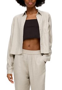 Light beige, cropped button-up shirt with long sleeves and a chest pocket, paired with a black cropped tank top and matching beige pants.