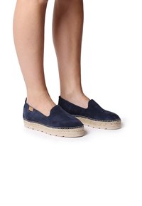 Marineblauwe suède instapschoenen met een jute zool en contrasterende stiksel rondom de basis; lichtgewicht en plat ontwerp, casual stijl.