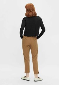 Czarna prążkowana bluzka z długim rękawem w połączeniu z beżowymi spodniami o prostych nogawkach z bocznymi rozcięciami, noszona z jasnymi mokasynami.