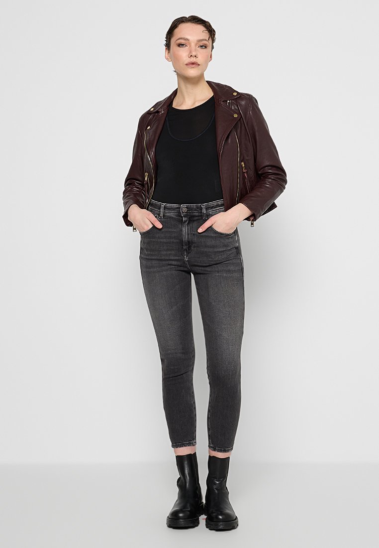 Burgunderrote Leder-Bikerjacke, enges schwarzes Oberteil, graue Skinny-Jeans und schwarze Knöchelboots; glatte Textur, Reißverschluss und taillierte Passform.