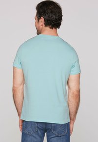 Svetlo modra kratka majica z kratkimi rokavi iz bombaža, ki ima okroglo izrez in enostaven dizajn, v kombinaciji z modrimi kavbojkami.