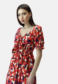 Rotes Blumenkleid mit Puffärmeln, quadratischem Ausschnitt und gerafftem Taillenbereich. Mit großen cremefarbenen und marineblauen Blumenmustern.