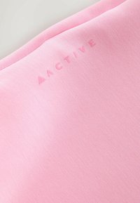 Hele roosa kangas sileda tekstuuriga, ülemises vasakus nurgas reljeefne „AACTIVE“ logo, mis viitab spordirõivastele.
