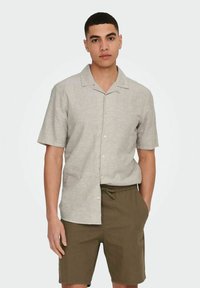 Camisa de lino de manga corta en gris claro con cuello y botones frontales, combinada con pantalones cortos verdes oliva con cintura con cordón.