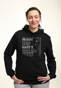 Svart hoodie i bomullsblandning med grafisk text "SVART ÄR MIN GLADA FÄRG." Designen inkluderar en huva med dragsko och ribbade ärmslut.