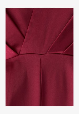 Zbliżenie na głęboki czerwony satynowy materiał z symetrycznymi fałdami i szwami tworzącymi gwiaździsty wzór.