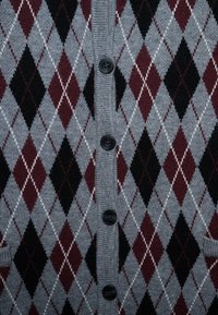 Grau karierter Cardigan mit roten, schwarzen und weißen Rauten im Argyle-Muster. Verfügt über einen gerippten Kragen und dunkle Knöpfe an der Vorderseite.