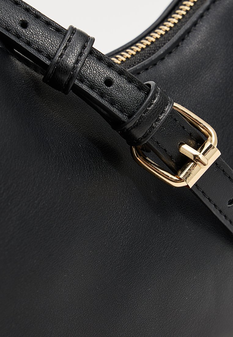 Detail van een zwarte leren tas met een textuur oppervlak, gouden hardware gesp en een rits langs de bovenrand.