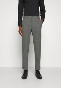 Pantaloni grigi su misura con una texture liscia, dotati di chiusura con bottone, tasche laterali e una vestibilità slim. Indossati con una camicia nera a maniche lunghe.