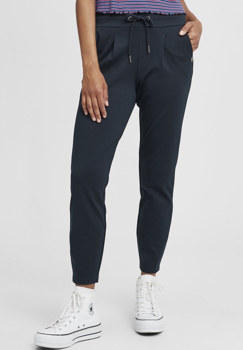 Marineblaue Jogginghosen mit Kordelzugbund, gefüttertem Vorderteil und Seitentaschen. Kombiniert mit weißen Sneakers im Hochmodell. Glattes, elastisches Material.