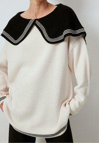 Strickpullover in Creme mit großem schwarzem Kragen mit weißen Streifen. Lockere Passform mit geripptem Saum und Bündchen. Weiche Textur.