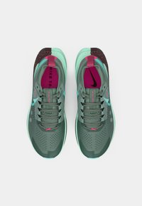 Egy tengerkék és rózsaszín Nike futócipő pár menta zöld részletekkel, felülnézetből, világos szürke háttér előtt.